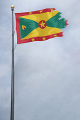 Worn and tattered Grenada flag blowing in the wind on a cloudy day