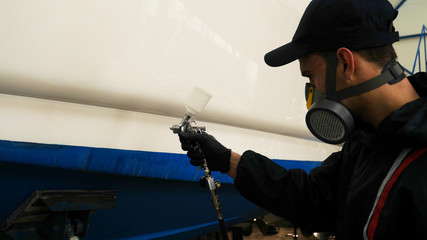 Professional master man in a robe and puller with spray gun puts a layer of paint or ceramics on the yacht. Concept of: Dangerous work, Chemistry, Paints, Garage, Transport Service.