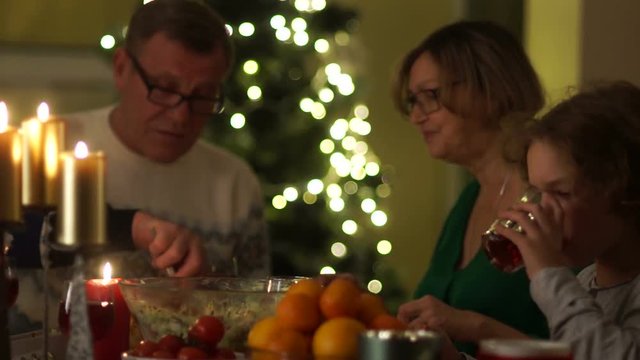 Christmas dinner by candlelight. The boy holds out a glass and he is poured a red compote from a jug. Happy family, christmas holidays