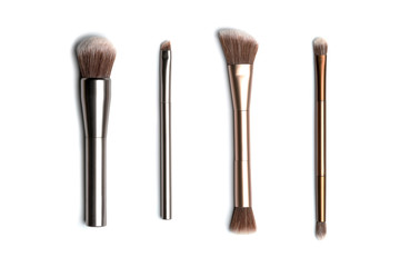 Four shiny bronze- and silver-coloured makeup brushes for applying powder, eyeshadow, eyeliner, bronzer and highlighter vertically arranged and shot from above with studio light on white background