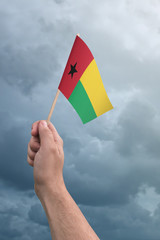 Hand holding Guinea Bissau flag high in the air, with a stormy, cloudy sky