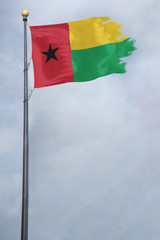 Fototapeta na wymiar Worn and tattered Guinea Bissau flag blowing in the wind on a cloudy day