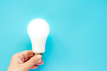 Hand holding glowing LED light bulb on blue background for energy savings concept