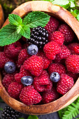 Freshly assorted berries in wooden bowl. Juicy and fresh blueberries6 blackberries and raspberries with green leaves on rustic background. Concept for healthy eating and nutrition.