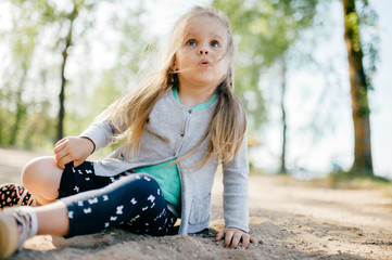 Little adorable beautiful child closeup portrait.  Young small girl with long hair and emotional expressive face mood outdoor summer portrait. Different facial expressions. Childhood.  Baby on road.