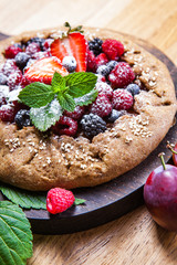 Whole-grain galette with plums and berries on dark background, top view