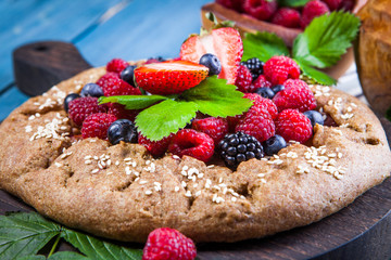 Whole-grain galette with plums and berries on dark background, top view