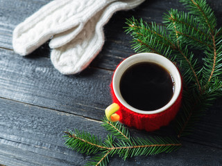 Coffee mug on a black wooden table with tree branches and warm wool mittens