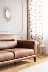 Bright living room interior with gold mirror, brown leather lounge and window with curtains in the real photo
