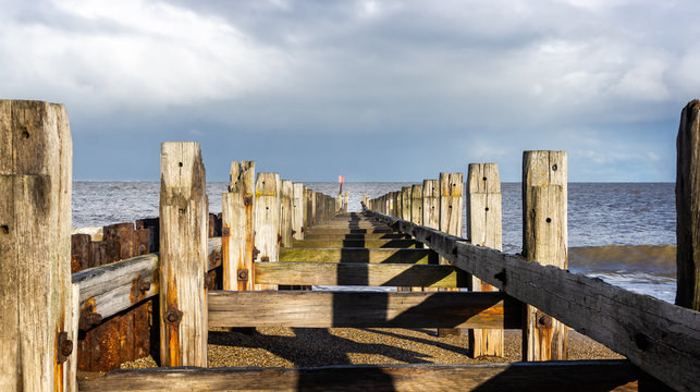 Dilapidated wooden groyne with two lines of wooden posts receding into the sea