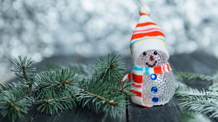 Snowman toy on the bokeh background with snowy tree branches and copy space