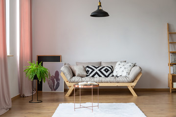 Copy space on the empty white wall in eclectic loft interior with beige scandinavian sofa and plant in pot