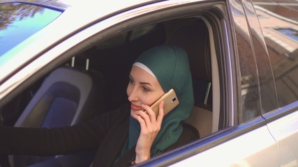 beautiful muslim woman driving a car talking on the phone smiling