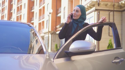 beautiful business woman muslim stands by car with telephone