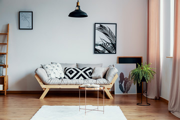 Patterned black and white pillow on beige scandinavian sofa in stylish interior with gallery of poster on the wall and white carpet on wooden floor, real photo