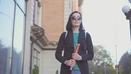 portrait of a blind girl in glasses with a cane on a city street