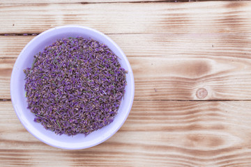 lavender dried scattered flowers in a white porcelain cup on wooden background, top view