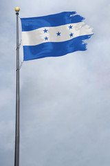 Worn and tattered Honduras flag blowing in the wind on a cloudy day