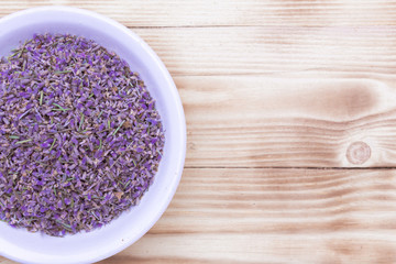 lavender dried scattered flowers in a white porcelain cup on wooden background, top view