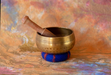 Closeup of a hammered-brass singing bowl with wood mallet and blue wool cushion.
