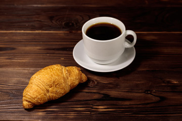 Cup of coffee and fresh croissant on wooden table