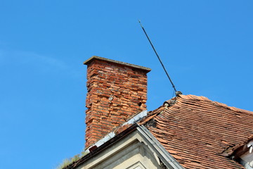 Cracked broken red brick chimney next to metal leaning lightning rod on top of abandoned old...