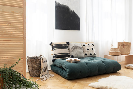Fur and basket next to green futon with pillows in boho bedroom interior with poster. Real photo