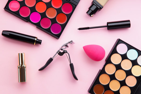 Top view picture of makeup products: lipstick and concealer palettes, foundation, mascara and eyelash curler on pink background. Feminine accessories concept