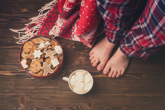 Female Feet Wearing Cozy Warm Pajamas Pants Jar with Gingerbread Cookies Cup of Hot Cococa with Marshmellow Cozy Christmas Concept Above Top View Toned Wooden Background