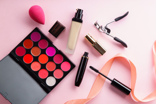 Top view picture of makeup products: lipstick palettes, foundation, mascara and eyelash curler on pink background. Make-up artist kit concept