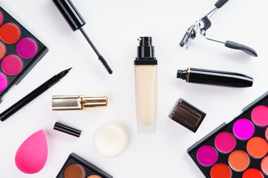 Overhead image of makeup products: lipstick and concealer palettes, foundation, mascara and eyelash curler on white background. Make-up artist kit concept