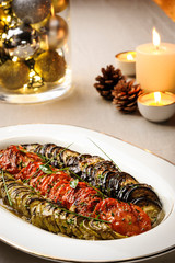 Delicious Ratatouille. Roasted zucchini with tomato and eggplant on a ceramic dish. Decorated table with candles and pine cone, on a cloth background
