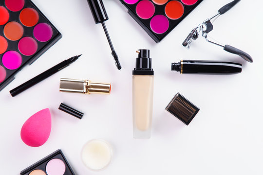Overhead image of makeup products: lipstick and concealer palettes, foundation, mascara and eyelash curler on white background. Make-up artist kit concept