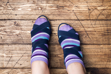 Women's feet in socks and sandals on wooden background.