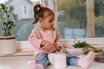 Little girl sitting on kitchen counter and playing with food,with the blurred backyard in back