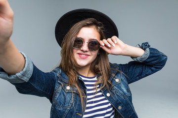 Cheerful young woman in hat and sunglasses taking a selfie isolated over white background