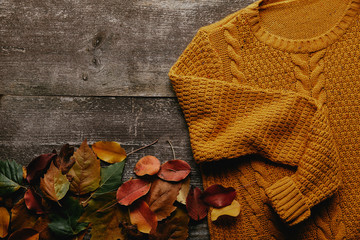 flat lay with fallen leaves and orange sweater on wooden tabletop - obrazy, fototapety, plakaty