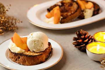 Delicious French Toast served with peach and ice cream on a ceramic dish. Decorated table with candles and pine cone, on a cloth background