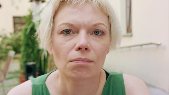 A pretty young blonde woman wearing a green dress sitting outside with a worried look on her face. Close-up shot