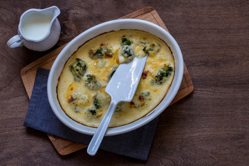 gratin with broccoli in white oval shape on wooden cutting Board