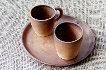 Obraz na płótnie Canvas Clay coffee cups and handmade ceramic dish on a rough homespun jute background.