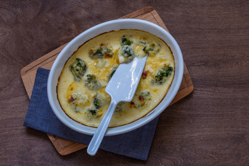 gratin with broccoli in white oval shape on wooden chopping Board on wooden background
