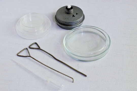 Retro. Glass Petri dishes, metal spirit lamp, metal loops and plastic pipette for the collection of biological fluids for bacteriological research on white gauze. Black and white photography.