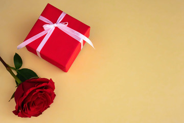 Red gift box with red rose on yellow background. Copy space.