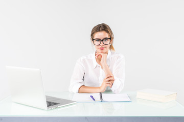 Young business woman sitting in front of a laptop with hands on chin at her office desk isolated on white background