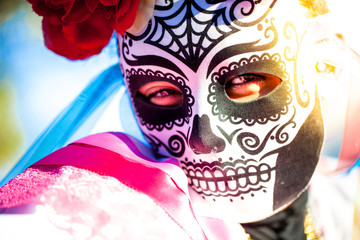 Woman wearing skull mask and paper flowers for Dia de Los Muertos/Day of the Dead