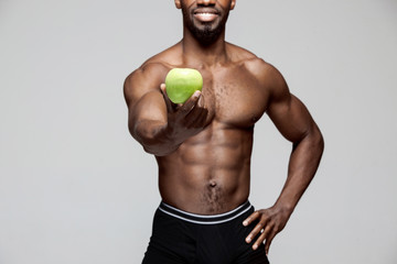 Fit young man with beautiful torso with green apple isolated on gray background. The naked torso of...