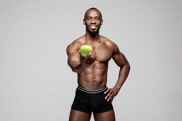 Fototapeta na wymiar Fit young man with beautiful torso with green apple isolated on gray background. The naked torso of African American man posing at studio. The body, fitness, sports, healthy lifestyle and bodybuilder