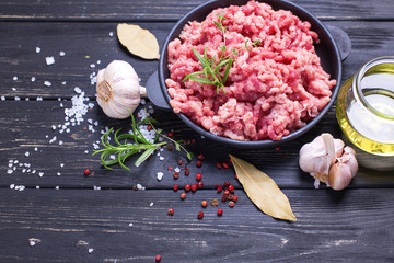 Raw minced meat in bowl  with ingredients for cooking on  black table.