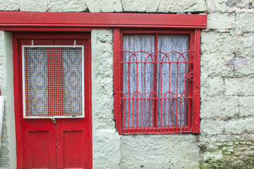 Fototapeta na wymiar old red door and window with red iron work on a whitewashed stone house